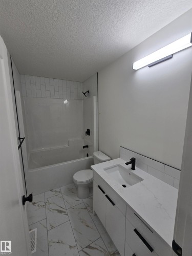 Full bath featuring vanity, a textured ceiling, shower / bath combination, and light marble finish flooring - 7706 174A Avenue, Edmonton, AB - Indoor Photo Showing Bathroom
