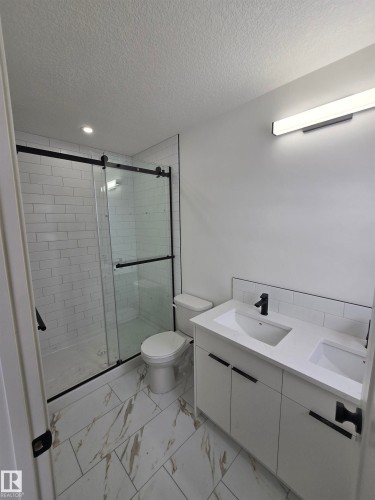 Full bathroom with double vanity, a textured ceiling, a stall shower, light marble finish flooring, and recessed lighting - 7706 174A Avenue, Edmonton, AB - Indoor Photo Showing Bathroom
