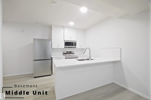 Kitchen with stainless steel appliances, backsplash, white cabinetry, a peninsula, and light stone countertops - 7585 174A Avenue, Edmonton, AB - Indoor Photo Showing Kitchen
