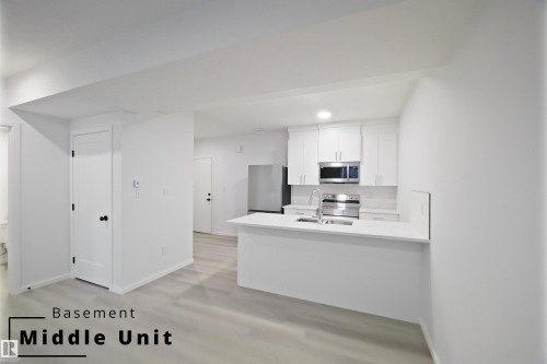 Kitchen with white cabinets, a peninsula, appliances with stainless steel finishes, decorative backsplash, and light stone countertops - 7585 174A Avenue, Edmonton, AB - Indoor Photo Showing Kitchen