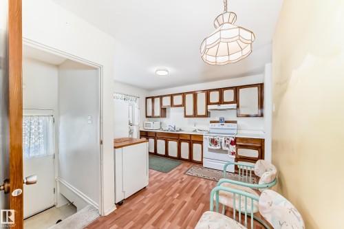 Kitchen featuring brown cabinets, white appliances, light countertops, hanging light fixtures, and white cabinets - Edmonton, AB - Indoor