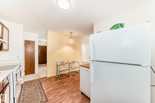 Kitchen with white appliances, decorative light fixtures, light wood-type flooring, and light countertops - Edmonton, AB - Indoor Photo Showing Kitchen