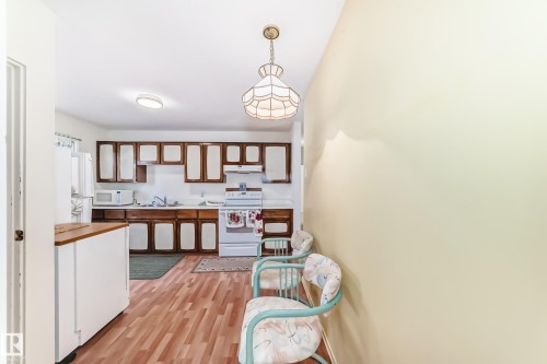 Kitchen with white appliances, hanging light fixtures, white cabinets, light countertops, and brown cabinets - Edmonton, AB - Indoor