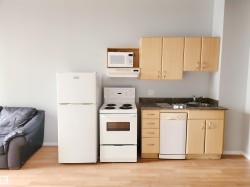 Kitchen with white appliances, light brown cabinets, under cabinet range hood, and light wood-style flooring - 