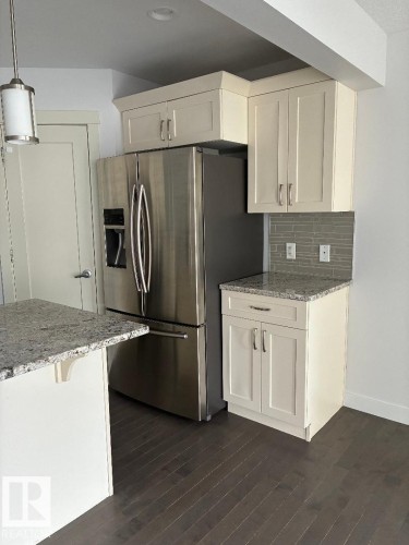 Kitchen featuring light stone countertops, stainless steel refrigerator with ice dispenser, decorative backsplash, and dark wood-type flooring - 2433 Glenridding Boulevard, Edmonton, AB - Indoor Photo Showing Kitchen