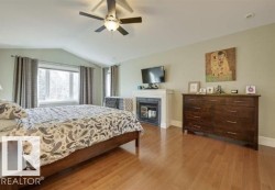 Bedroom featuring lofted ceiling, light wood-style flooring, a glass covered fireplace, and ceiling fan - 