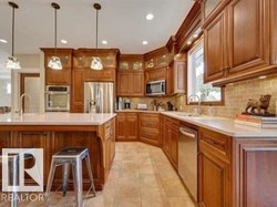 Kitchen featuring decorative light fixtures, a breakfast bar, brown cabinets, glass insert cabinets, and appliances with stainless steel finishes - 