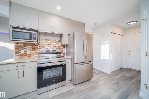 Kitchen featuring stainless steel appliances, backsplash, light wood-type flooring, under cabinet range hood, and light stone countertops - 3504 20 Street, Edmonton, AB - Indoor Photo Showing Kitchen