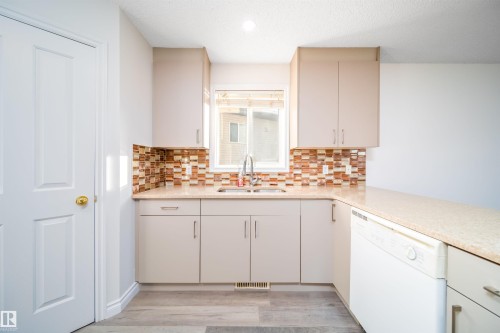 Kitchen featuring dishwasher, light wood-type flooring, a textured ceiling, backsplash, and light stone countertops - 3504 20 Street, Edmonton, AB - Indoor Photo Showing Kitchen With Double Sink