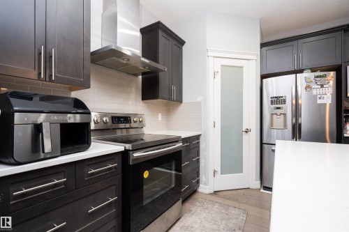 Kitchen featuring stainless steel appliances, wall chimney range hood, decorative backsplash, and light wood-type flooring - 2060 Ware Road, Edmonton, AB - Indoor Photo Showing Kitchen