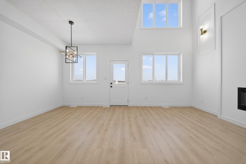 Entryway featuring light wood-style flooring, plenty of natural light, a glass covered fireplace, hanging lights, and a high textured ceiling - 129 Pierwyck Loop, Spruce Grove, AB - Indoor Photo Showing Other Room With Fireplace