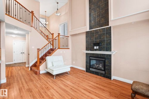 Living room featuring a towering ceiling, a tile fireplace, wood finished floors, and stairs - 1888 33 Street, Edmonton, AB - Indoor With Fireplace