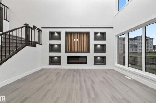 Unfurnished living room with built in features, light wood finished floors, a towering ceiling, and healthy amount of natural light - 3164 Magpie Way, Edmonton, AB - Indoor With Fireplace