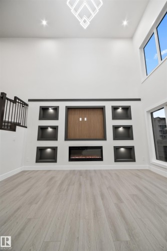Unfurnished living room with built in features, light wood-style floors, a towering ceiling, a glass covered fireplace, and recessed lighting - 3164 Magpie Way, Edmonton, AB - Indoor Photo Showing Other Room