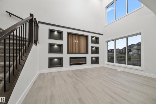 Unfurnished living room with light wood-type flooring, built in shelves, stairway, a towering ceiling, and a glass covered fireplace - 3164 Magpie Way, Edmonton, AB - Indoor With Fireplace