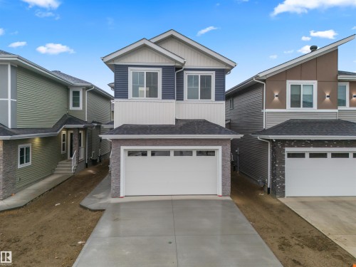 View of front facade with board and batten siding, driveway, a garage, a shingled roof, and brick siding - 3164 Magpie Way, Edmonton, AB - Outdoor With Facade