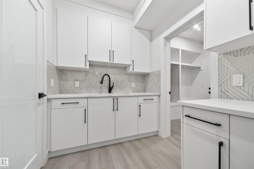 Kitchen featuring white cabinets, light wood-style floors, decorative backsplash, and light stone countertops - 3164 Magpie Way, Edmonton, AB - Indoor Photo Showing Kitchen