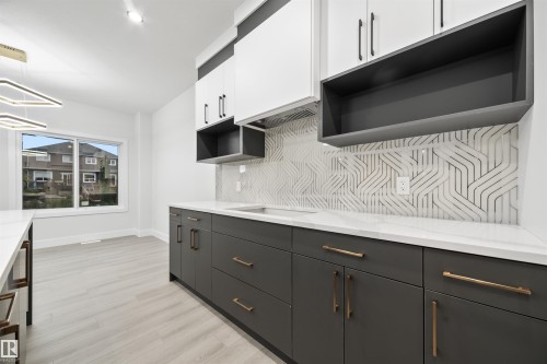 Kitchen featuring backsplash, white cabinets, light wood-style floors, open shelves, and light stone countertops - 3164 Magpie Way, Edmonton, AB - Indoor Photo Showing Kitchen
