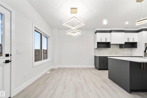 Kitchen with white cabinets, decorative backsplash, pendant lighting, light wood-style flooring, and dark cabinets - 3164 Magpie Way, Edmonton, AB - Indoor Photo Showing Kitchen