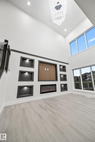 Unfurnished living room featuring built in shelves, a towering ceiling, light wood-style flooring, a glass covered fireplace, and recessed lighting - 3164 Magpie Way, Edmonton, AB - Indoor Photo Showing Other Room With Fireplace