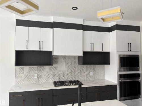 Kitchen featuring stainless steel appliances, white cabinetry, dark cabinets, light stone countertops, and backsplash - 3164 Magpie Way, Edmonton, AB - Indoor Photo Showing Kitchen