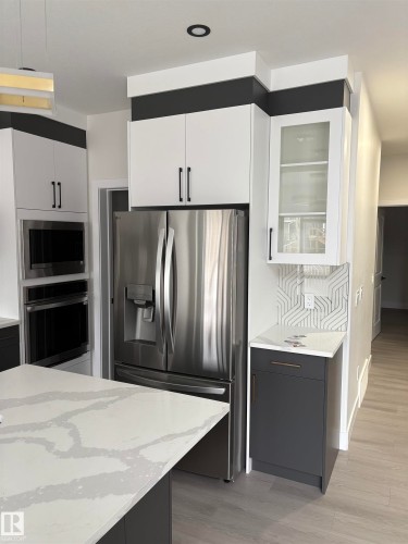 Kitchen featuring stainless steel appliances, light stone countertops, white cabinetry, glass insert cabinets, and dark cabinets - 3164 Magpie Way, Edmonton, AB - Indoor Photo Showing Kitchen