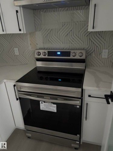 Kitchen with stainless steel electric range oven, white cabinets, under cabinet range hood, backsplash, and light stone counters - 3164 Magpie Way, Edmonton, AB - Indoor Photo Showing Kitchen