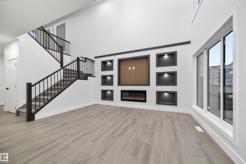 Unfurnished living room with light wood finished floors, a high ceiling, stairs, and a glass covered fireplace - 3164 Magpie Way, Edmonton, AB - Indoor Photo Showing Other Room With Fireplace