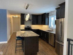 Kitchen featuring appliances with stainless steel finishes, hanging light fixtures, light stone countertops, a center island, and a breakfast bar area - 