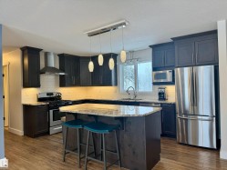 Kitchen featuring appliances with stainless steel finishes, decorative backsplash, hanging light fixtures, wall chimney range hood, and a breakfast bar - 