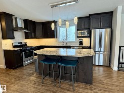 Kitchen with appliances with stainless steel finishes, wall chimney exhaust hood, light stone counters, pendant lighting, and a breakfast bar area - 