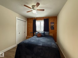 Bedroom with wooden walls, a closet, dark wood finished floors, and a ceiling fan - 