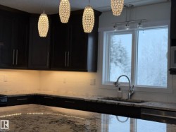 Kitchen with dark cabinetry, light stone counters, dishwasher, decorative light fixtures, and tasteful backsplash - 