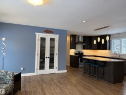 Kitchen with a kitchen breakfast bar, appliances with stainless steel finishes, light stone countertops, pendant lighting, and wall chimney exhaust hood - 