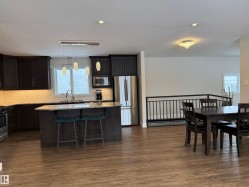 Kitchen with stainless steel appliances, light stone countertops, a kitchen breakfast bar, a kitchen island, and hanging light fixtures - 