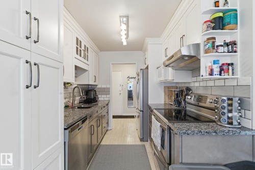 Kitchen featuring appliances with stainless steel finishes, dark stone countertops, under cabinet range hood, white cabinets, and light wood-style flooring - 205 11440 40 Ave, Edmonton, AB - Indoor Photo Showing Kitchen With Stainless Steel Kitchen
