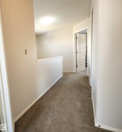 Hallway featuring a textured ceiling, dark carpet, and an upstairs landing - 