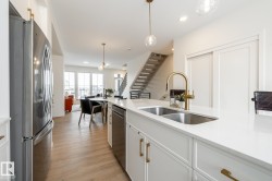 Kitchen featuring appliances with stainless steel finishes, white cabinetry, light wood finished floors, pendant lighting, and light stone countertops - 