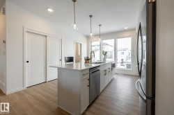 Kitchen with white cabinets, stainless steel appliances, a center island with sink, hanging light fixtures, and light wood-type flooring - 