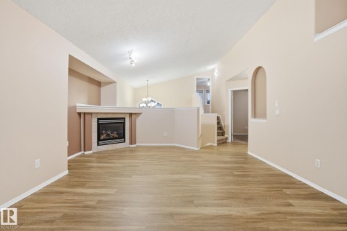 Unfurnished living room featuring stairway, lofted ceiling, a chandelier, light wood-style flooring, and a tiled fireplace - 3316 24 Avenue, Edmonton, AB - Indoor With Fireplace