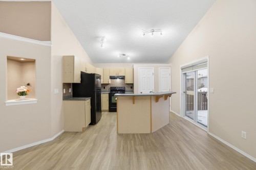 Kitchen featuring lofted ceiling, a kitchen breakfast bar, black appliances, light brown cabinets, and a center island - 3316 24 Avenue, Edmonton, AB - Indoor Photo Showing Kitchen