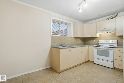 Kitchen with white electric stove, under cabinet range hood, light countertops, tasteful backsplash, and light tile patterned floors - 3316 24 Avenue, Edmonton, AB - Indoor Photo Showing Kitchen With Double Sink