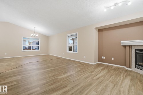 Unfurnished living room featuring a chandelier, light wood-style floors, a tiled fireplace, lofted ceiling, and a textured ceiling - 3316 24 Avenue, Edmonton, AB - Indoor With Fireplace