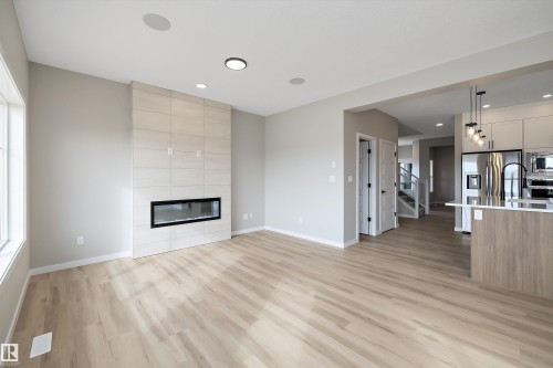 Unfurnished living room featuring a tile fireplace, stairs, light wood-style floors, and recessed lighting - 4544 Kinsella Link, Edmonton, AB - Indoor With Fireplace
