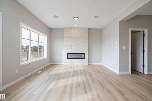 Unfurnished living room with light wood-style floors, a fireplace, a residential view, and recessed lighting - 4544 Kinsella Link, Edmonton, AB - Indoor Photo Showing Living Room With Fireplace