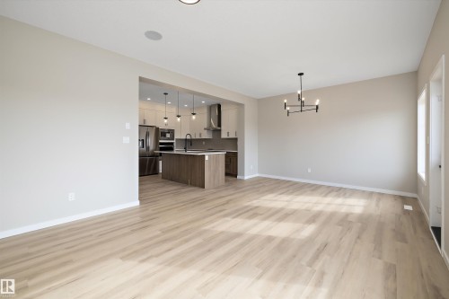 Kitchen featuring open floor plan, a center island with sink, pendant lighting, stainless steel appliances, and wall chimney exhaust hood - 4544 Kinsella Link, Edmonton, AB - Indoor
