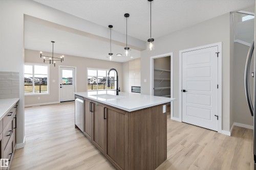 Kitchen featuring hanging light fixtures, a kitchen island with sink, light wood-type flooring, light stone counters, and a chandelier - 4544 Kinsella Link, Edmonton, AB - Indoor Photo Showing Kitchen With Upgraded Kitchen