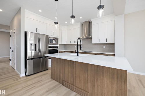 Kitchen featuring stainless steel appliances, white cabinets, light wood-style flooring, a center island with sink, and backsplash - 4544 Kinsella Link, Edmonton, AB - Indoor Photo Showing Kitchen With Upgraded Kitchen