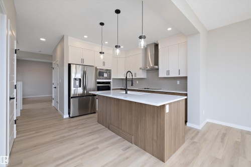 Kitchen featuring stainless steel appliances, white cabinets, backsplash, a center island with sink, and brown cabinetry - 4544 Kinsella Link, Edmonton, AB - Indoor Photo Showing Kitchen With Upgraded Kitchen