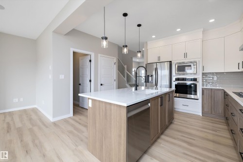 Kitchen featuring pendant lighting, stainless steel appliances, light wood-style floors, tasteful backsplash, and white cabinetry - 4544 Kinsella Link, Edmonton, AB - Indoor Photo Showing Kitchen With Upgraded Kitchen